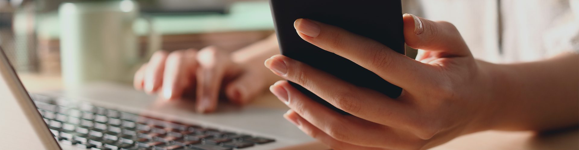 Kvindehånd holder telefon og arbejder med computer