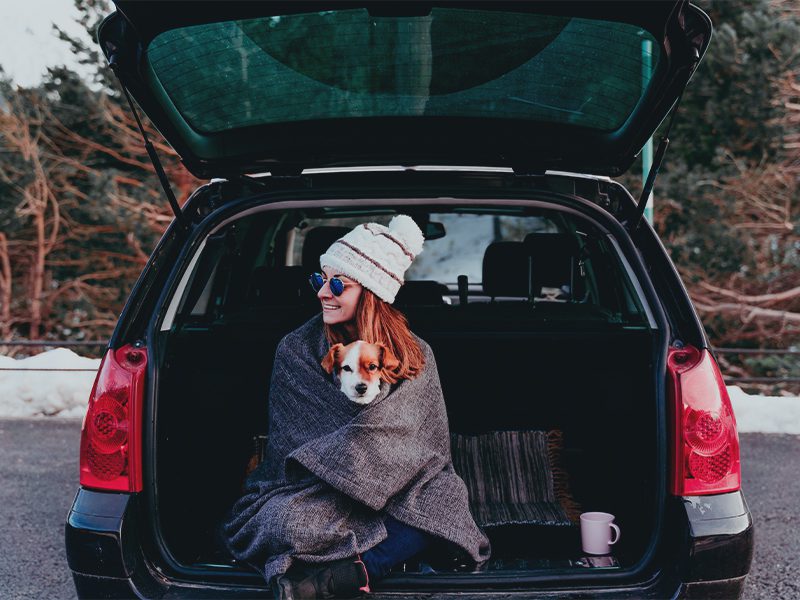 Kvinde sidder bag i bil med sin hund på skødet